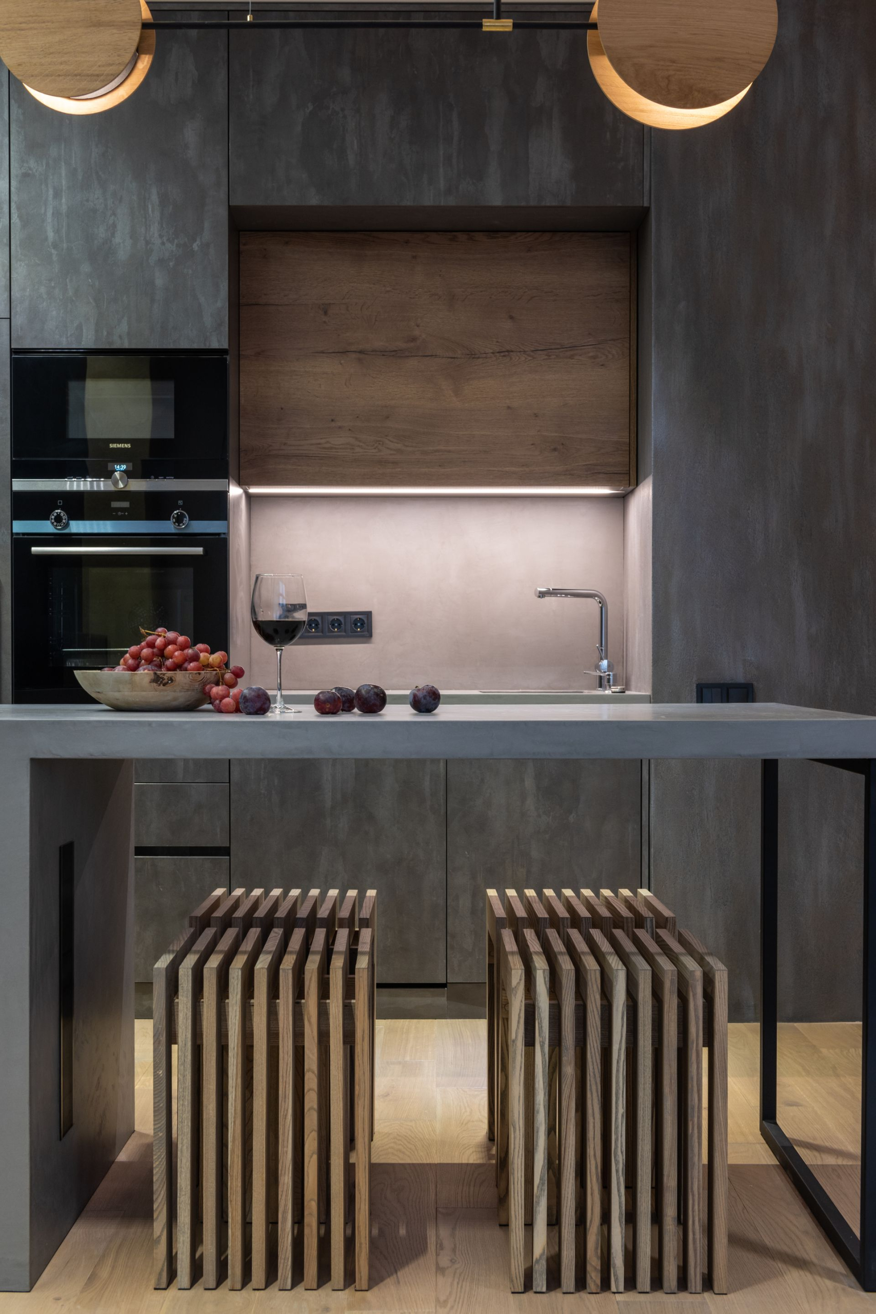 Compact kitchen with dark slate surfaces, a timber splashback panel and slatted timber stools